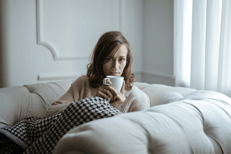 woman-sipping-coffee-on-couch-in-blanket-min